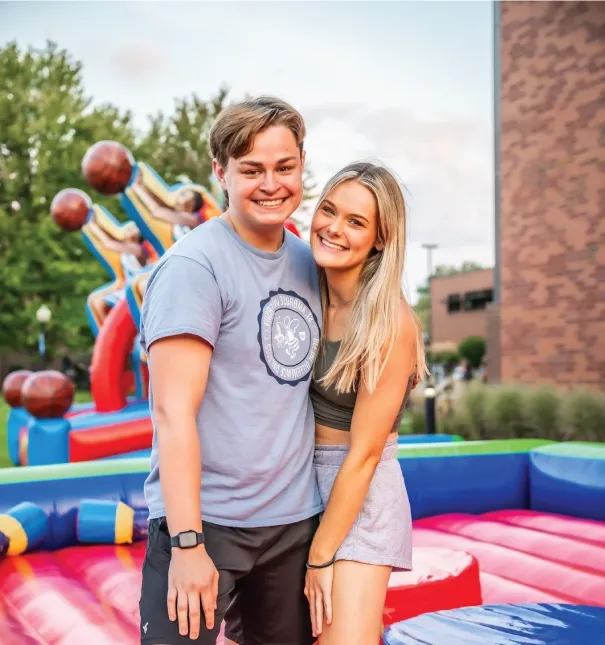 Two students smiling at an outdoor event standing on a bouncy platform.